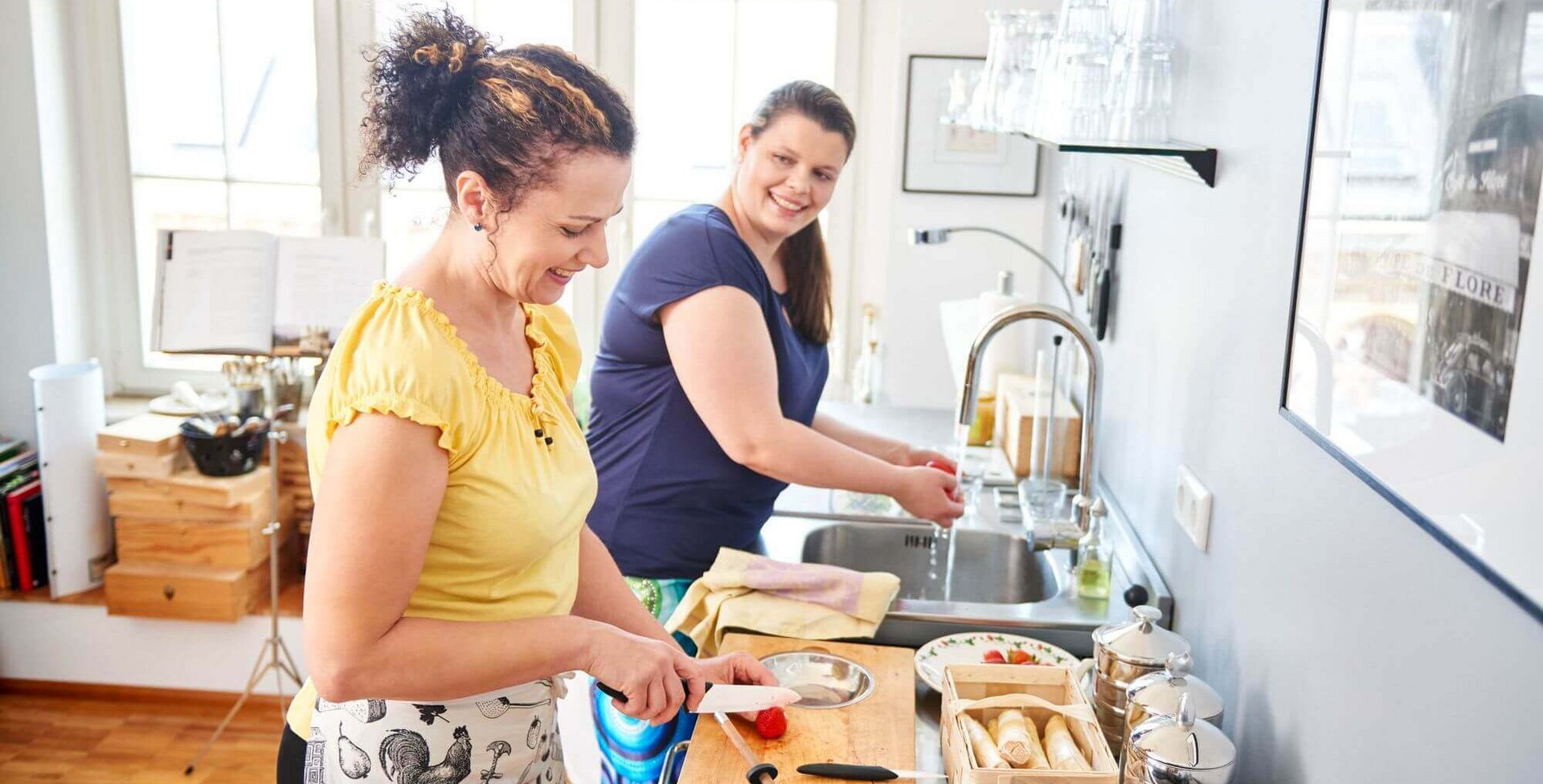 Zwei Frauen stehen in einer Küche und kochen zusammen. Eine gesunde und ausgewogene Ernährung ist sehr hilfreich bei der Behandlung von Lipolymphödemen.